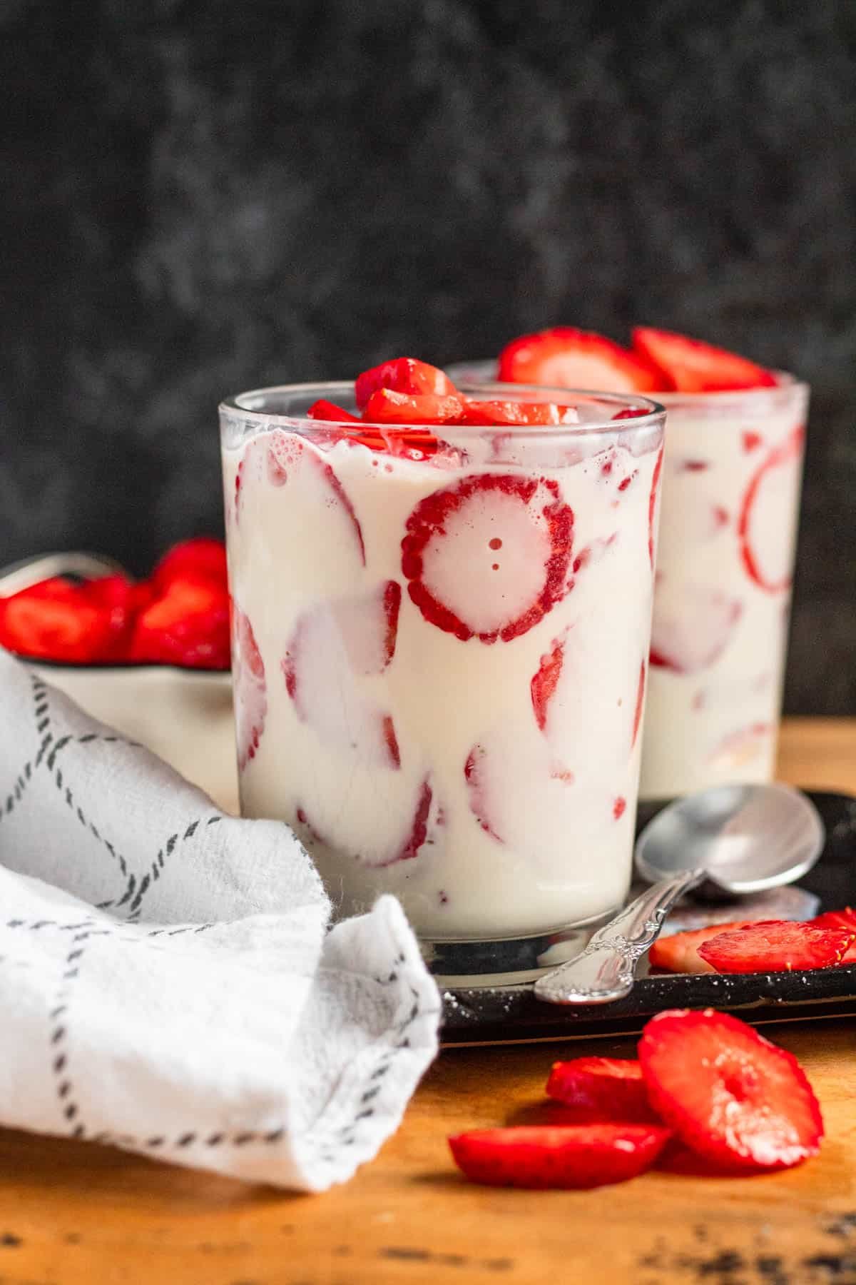 A glass filled with fresh strawberry slices topped with a generous spoonful of creamy crema.