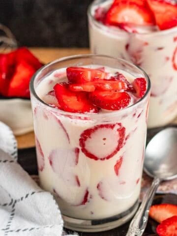 Glasses filled with creamy Fresas Con Crema mixed with fresh sliced strawberries.