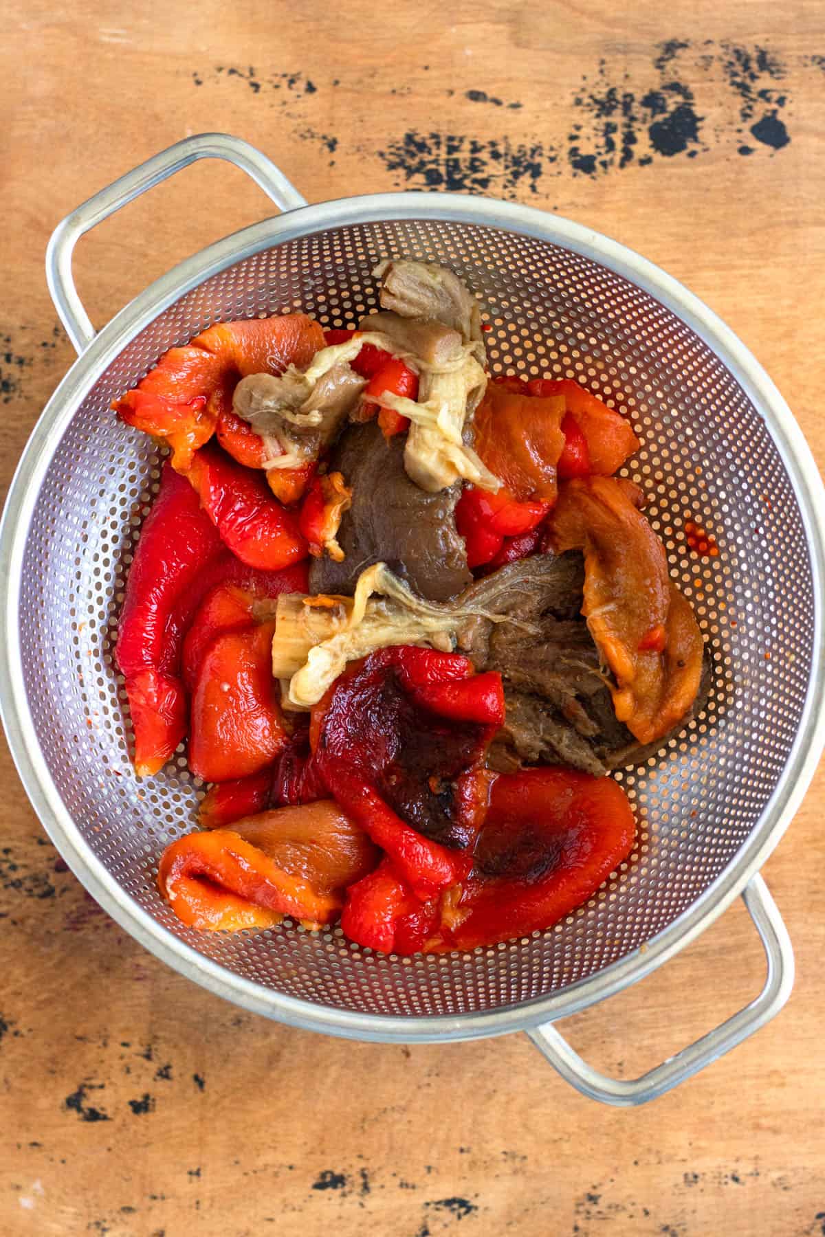 Peeled red bell peppers and eggplant rest in a colander.