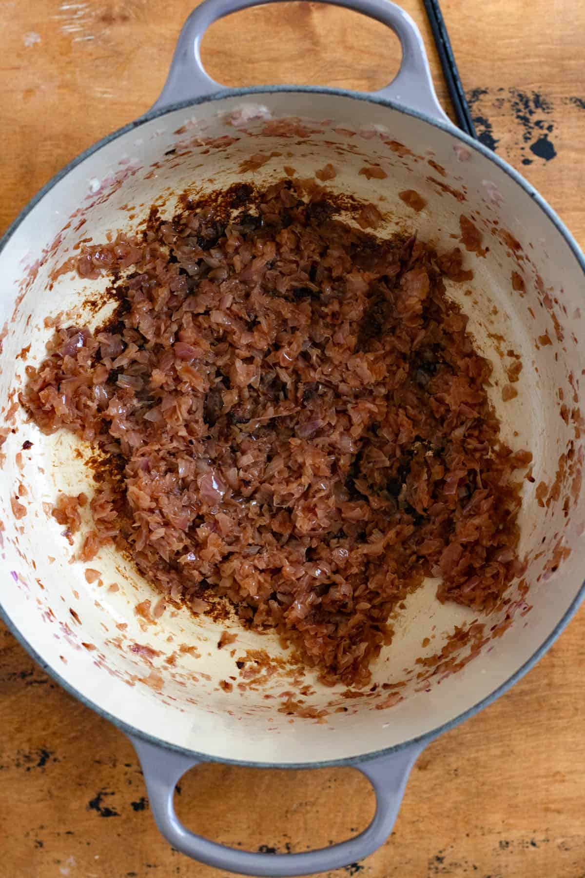 Onions in a Dutch oven being stirred with vegetable oil, ginger paste, garlic paste, and tomato paste.