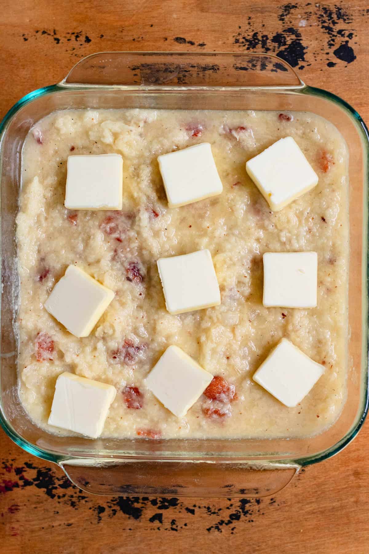 Potato mixture poured into a greased glass pan topped with butter slices.