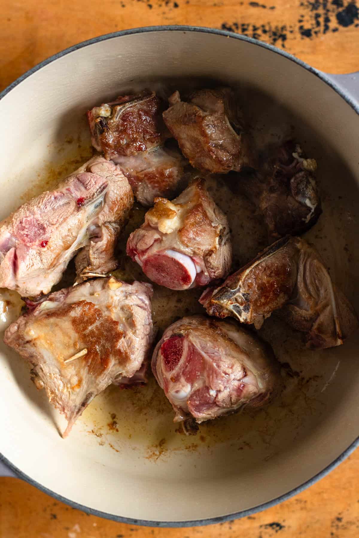 Lamb pieces are browned in ghee inside a Dutch oven.