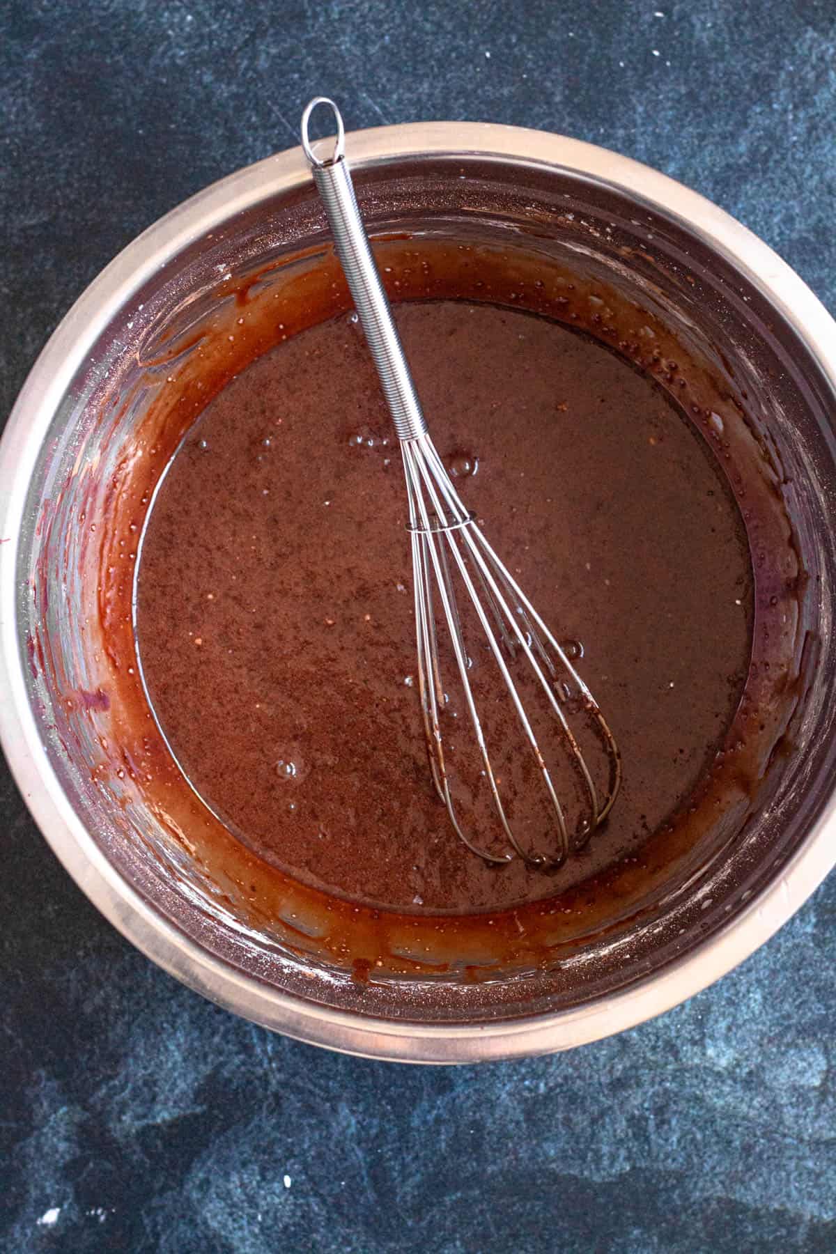 Cocoa powder being mixed into a bowl with melted butter, milk, powdered sugar, and salt to create chocolate icing.