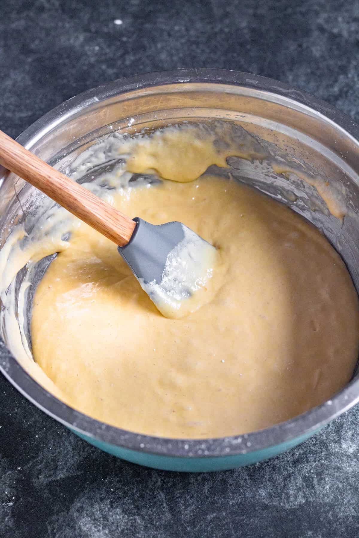 Spatula resting in a mixing bowl of batter for lamingtons. 