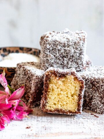 Lamingtons stacked together on a plate with bright pink flowers garnished on the side.