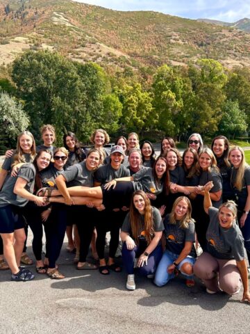 A group of girls in front of a mountain, holding up one smiling girl