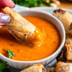 A bowl of creamy Thai peanut sauce with a crispy spring roll being dipped into it.