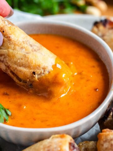 A bowl of creamy Thai peanut sauce with a crispy spring roll being dipped into it.