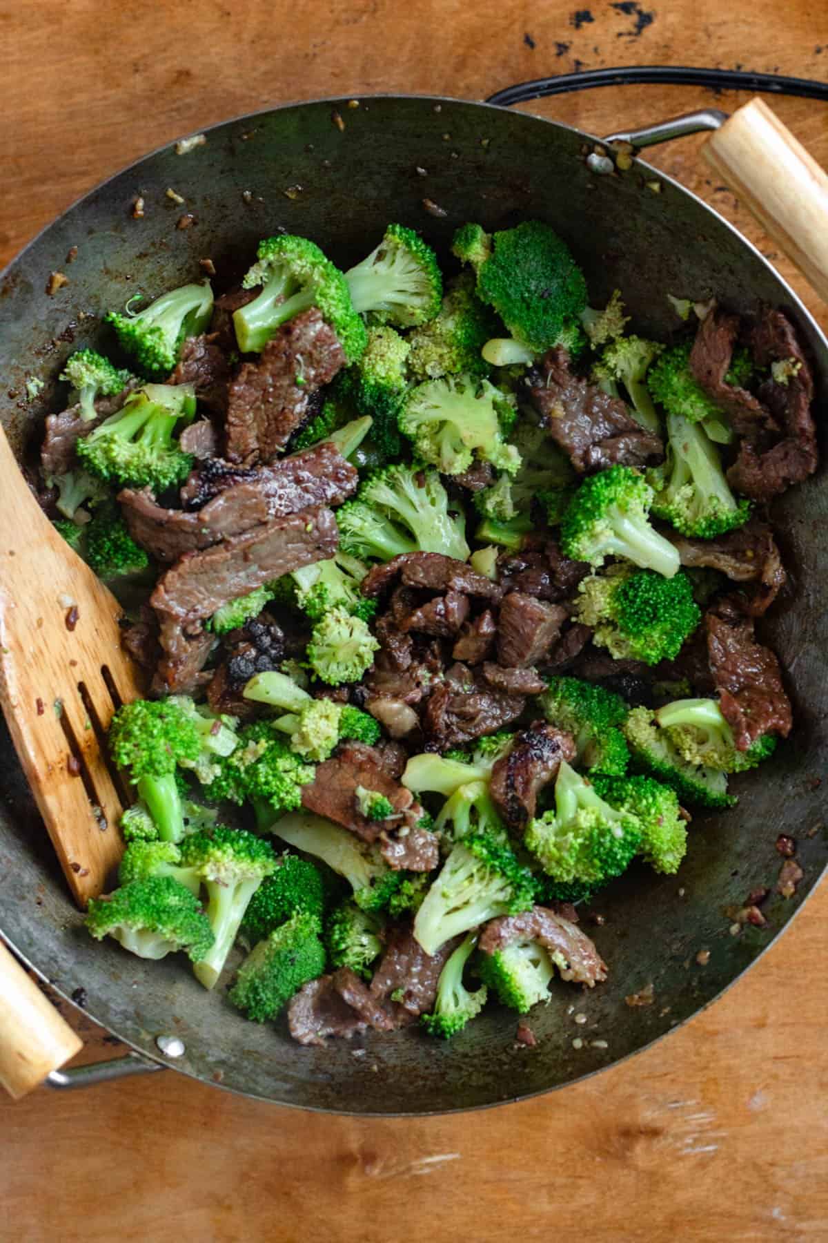 Broccoli being added to the wok and tossed together with the cooked beef.
