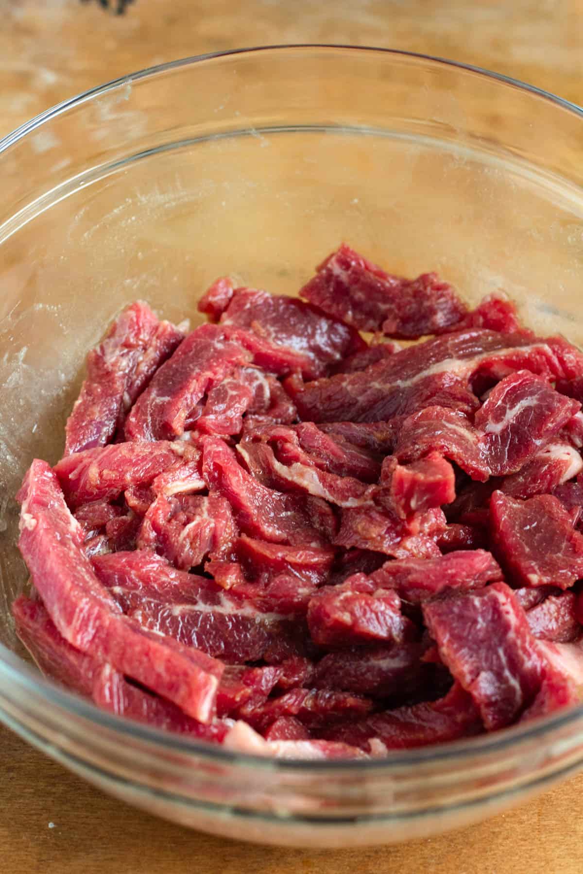 Marinade being poured over sliced flank steak in a bowl for marinating.
