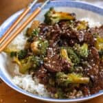 A bowl of beef and broccoli recipe served over white rice, topped with sesame seeds.