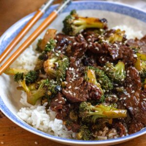 A bowl of beef and broccoli recipe served over white rice, topped with sesame seeds.