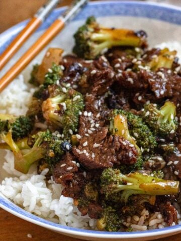 A bowl of beef and broccoli recipe served over white rice, topped with sesame seeds.