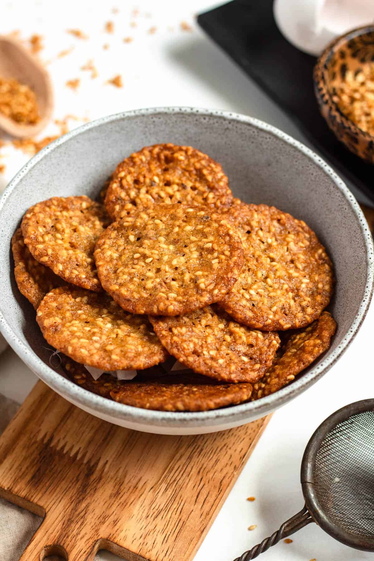 A bowl filled with crispy Benne Wafers on a wooden board.