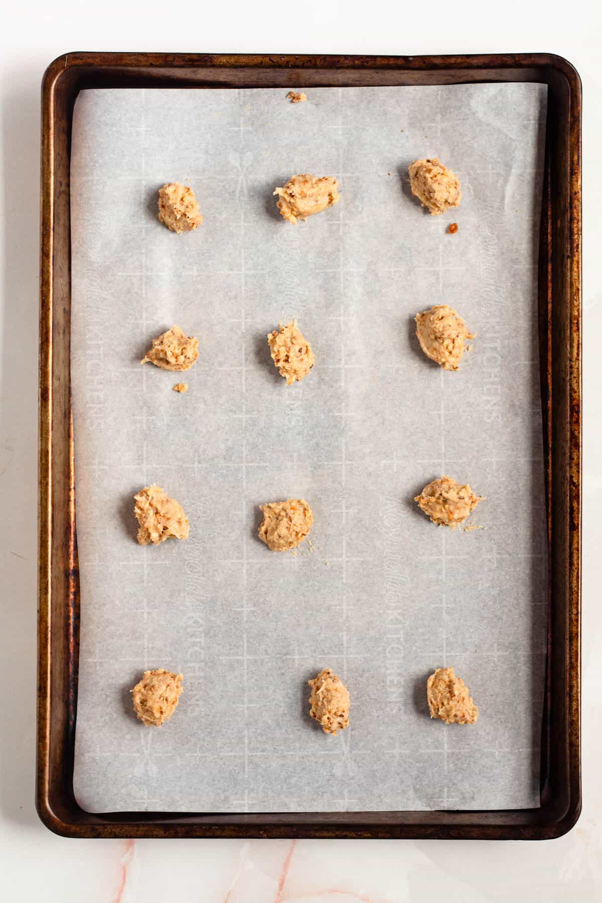 Cookie dough being spooned onto a parchment-lined baking sheet.
