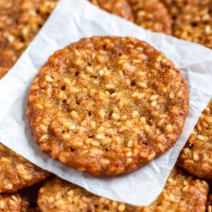 Crispy benne seed cookies stacked on parchment paper.