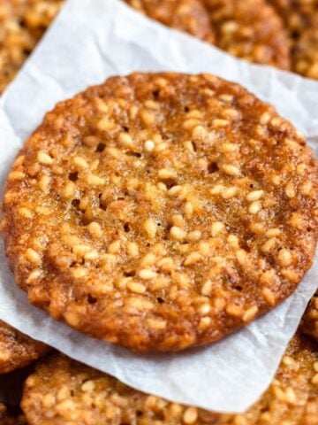 Crispy benne seed cookies stacked on parchment paper.