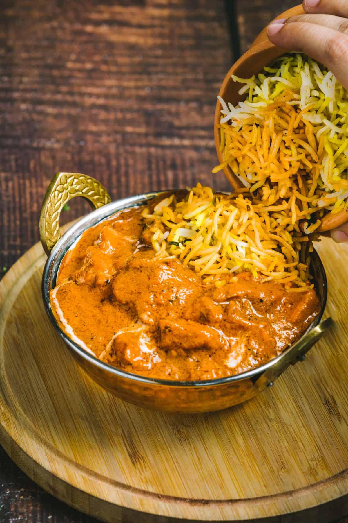 A bowl of creamy butter chicken topped with colorful basmati rice being poured in.