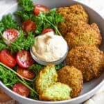Bowl of middle eastern falafel recipe with cherry tomatoes halved and a dipping sauce.