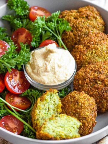 Bowl of middle eastern falafel recipe with cherry tomatoes halved and a dipping sauce.