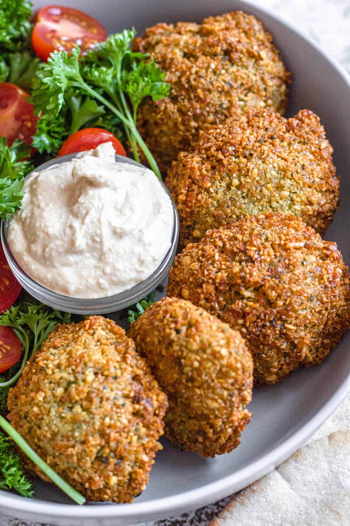 Crispy falafel served with creamy dip, cherry tomatoes, and fresh parsley in a bowl.