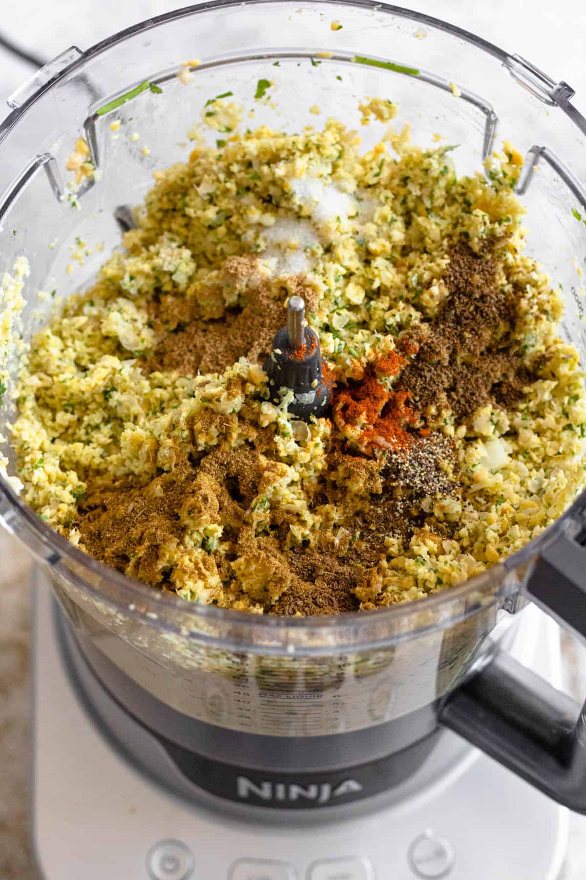 Blended chickpeas, herbs, onion, garlic, and spices in a food processor.