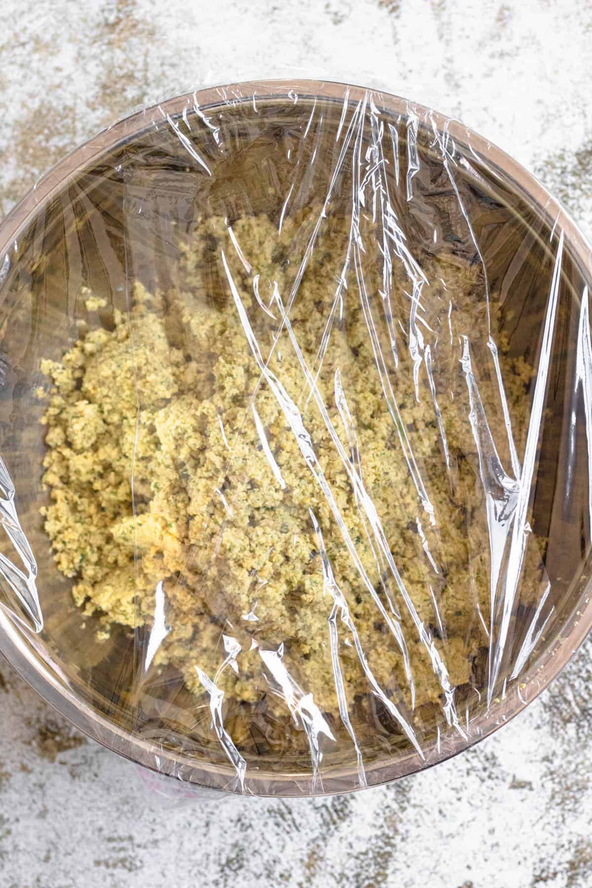 Falafel mixture covered with plastic wrap and left to chill in a bowl.
