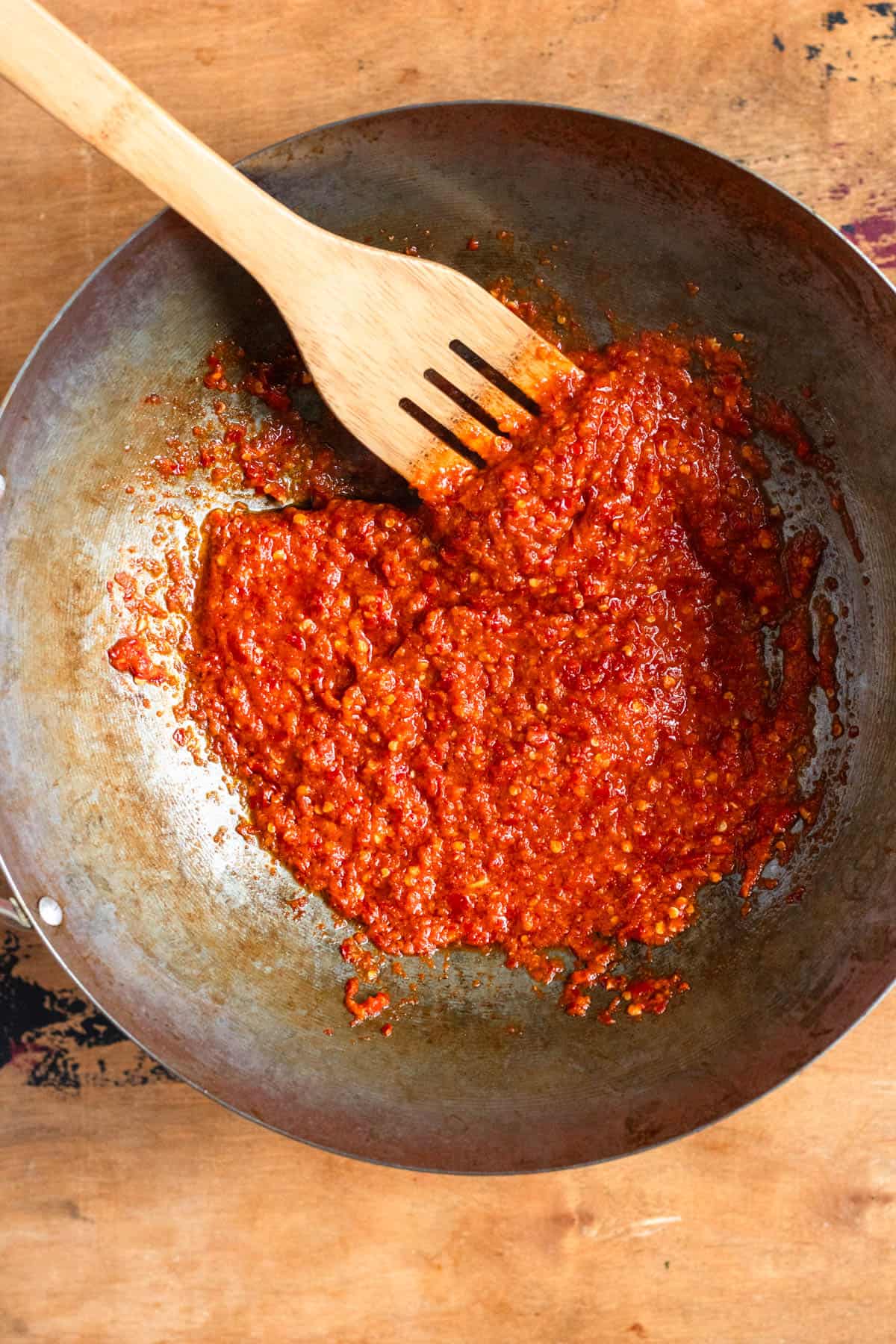 Sambal paste being poured into hot oil and fried in a pan.
