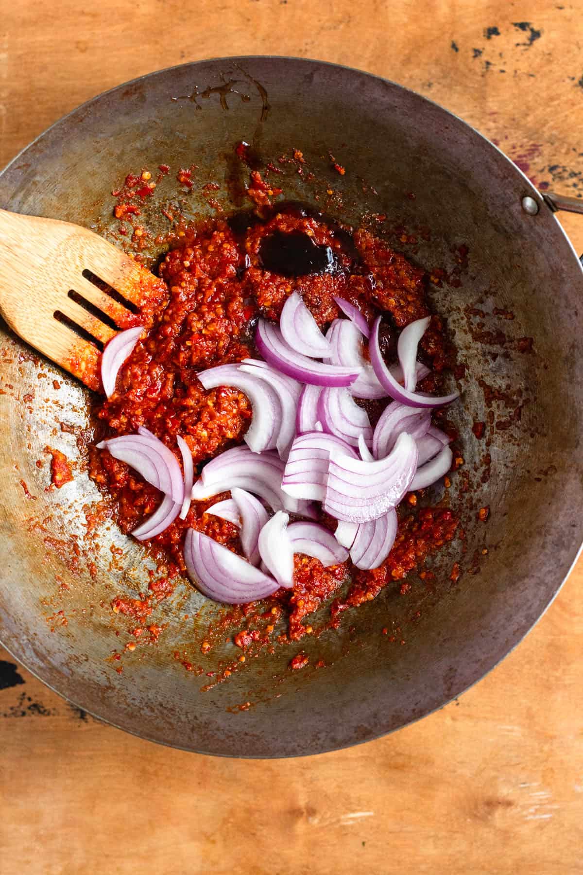 Tamarind paste, coconut sugar, salt, and sliced red onion added to a pan of sambal paste.