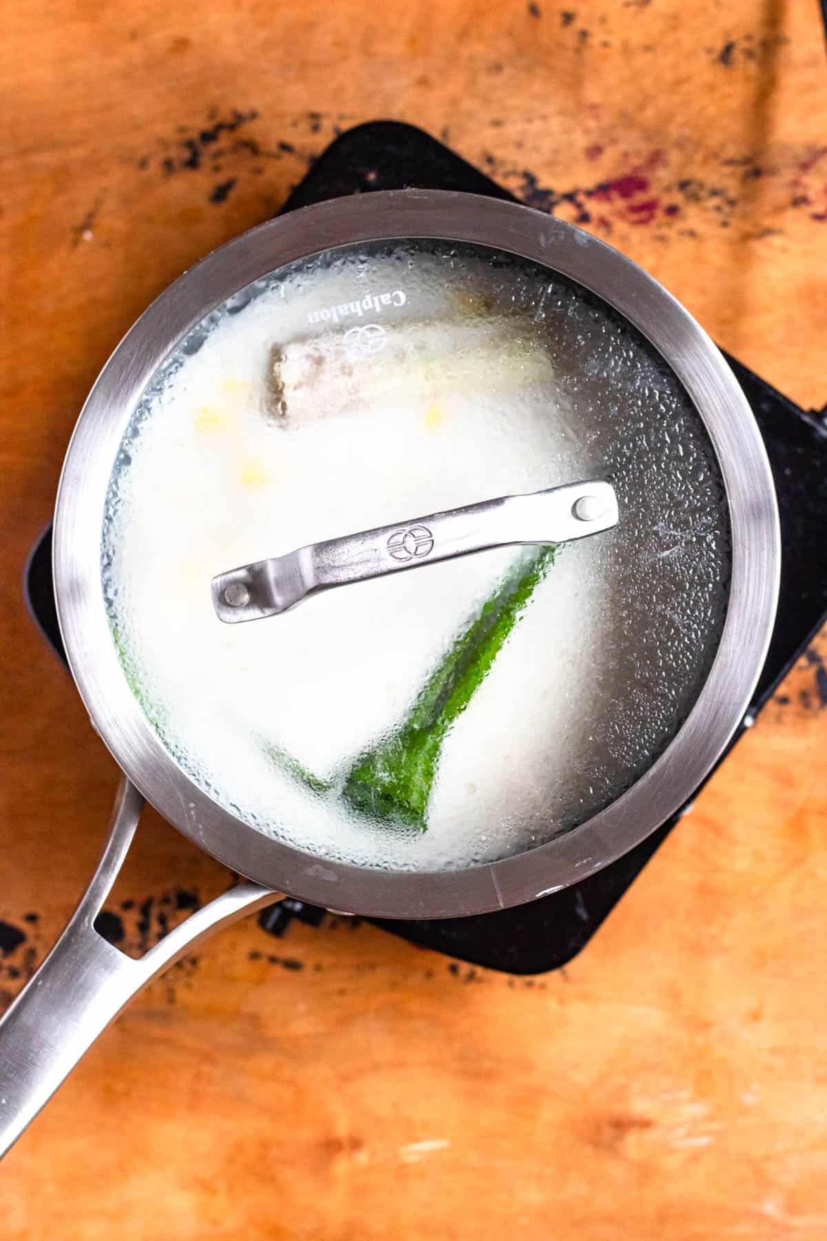 A pot filled with rice, coconut milk, pandan leaf, lemongrass, and salt ready to cook.