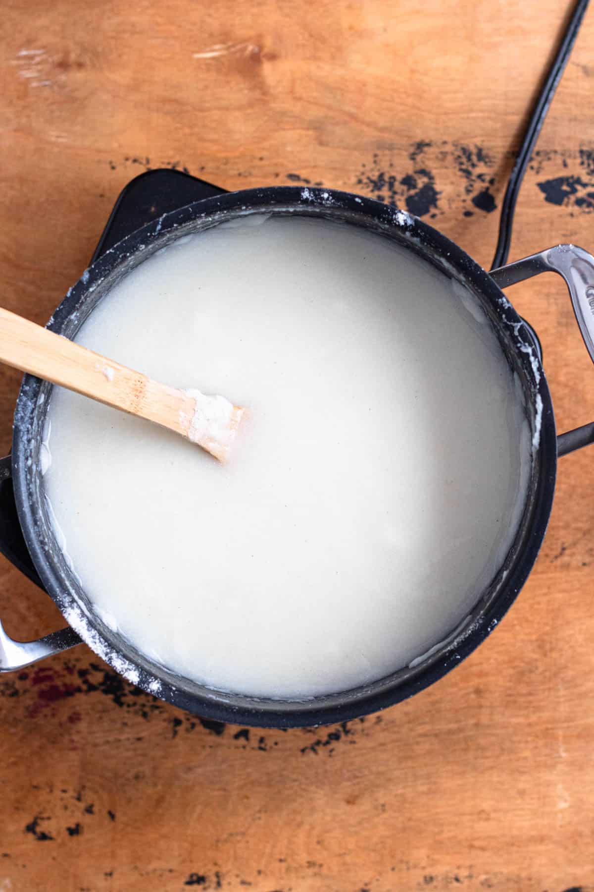 Cornmeal being stirred into hot water with a wooden spoon.