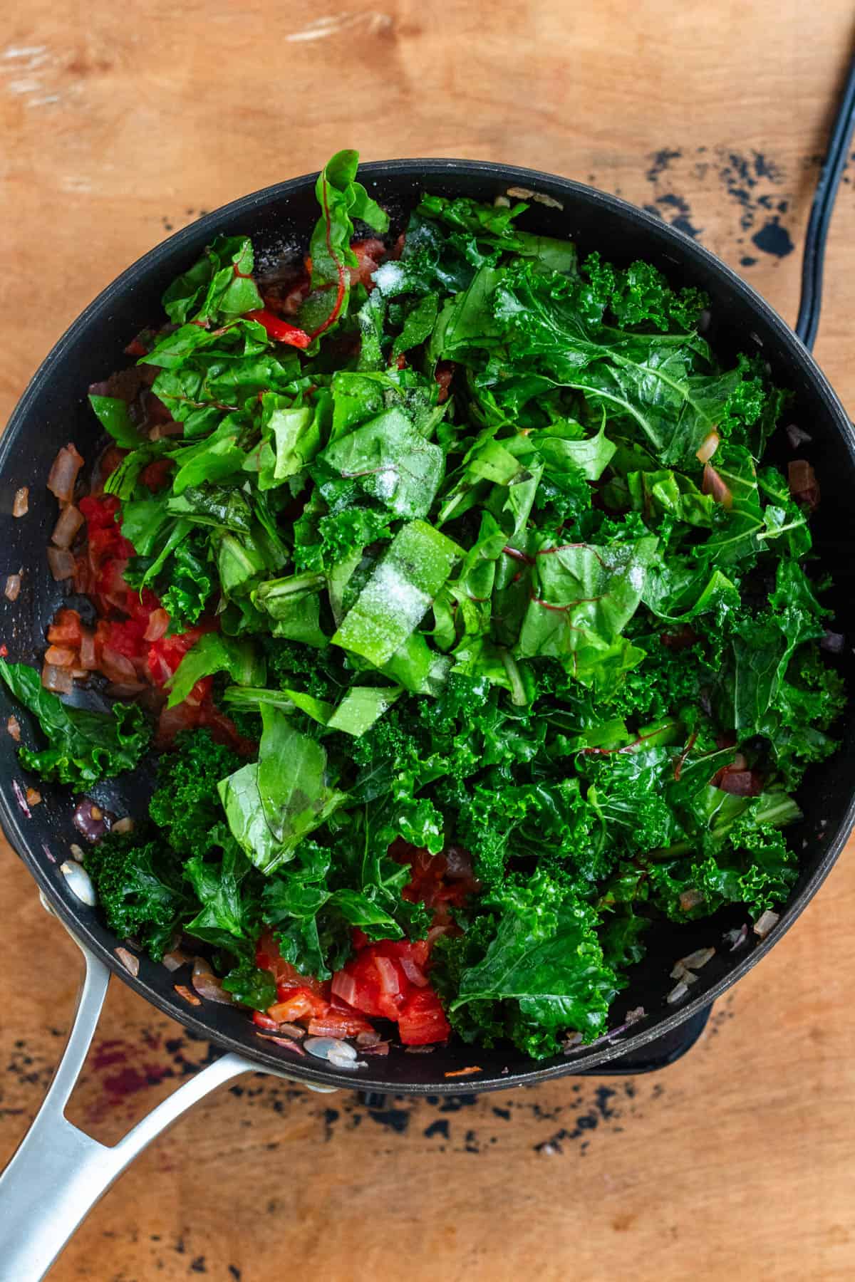 Kale, rainbow chard, and dandelion greens added to a pan of sautéed onions, garlic, and tomatoes.