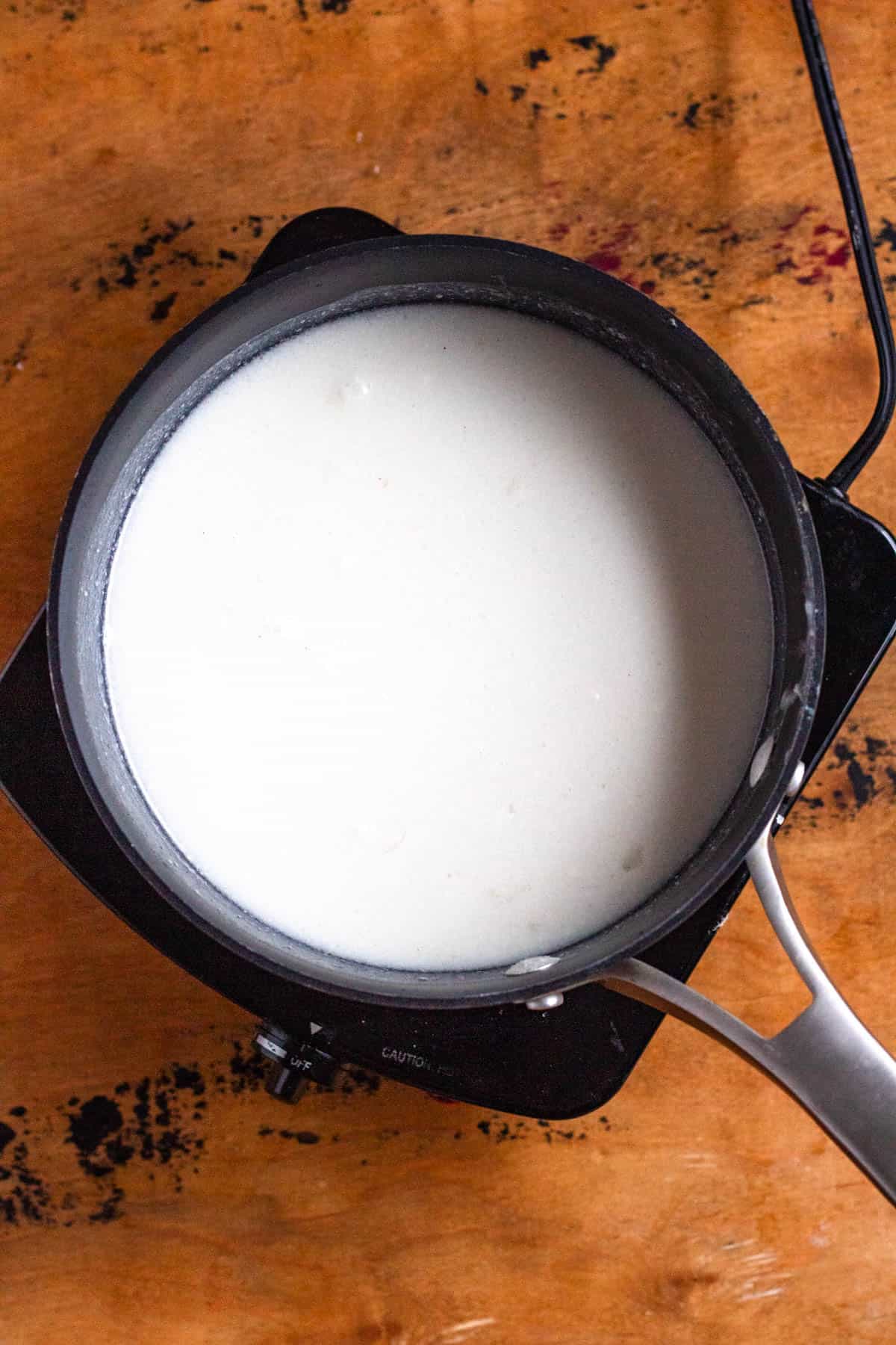 A pot of coconut milk heating on a stovetop.