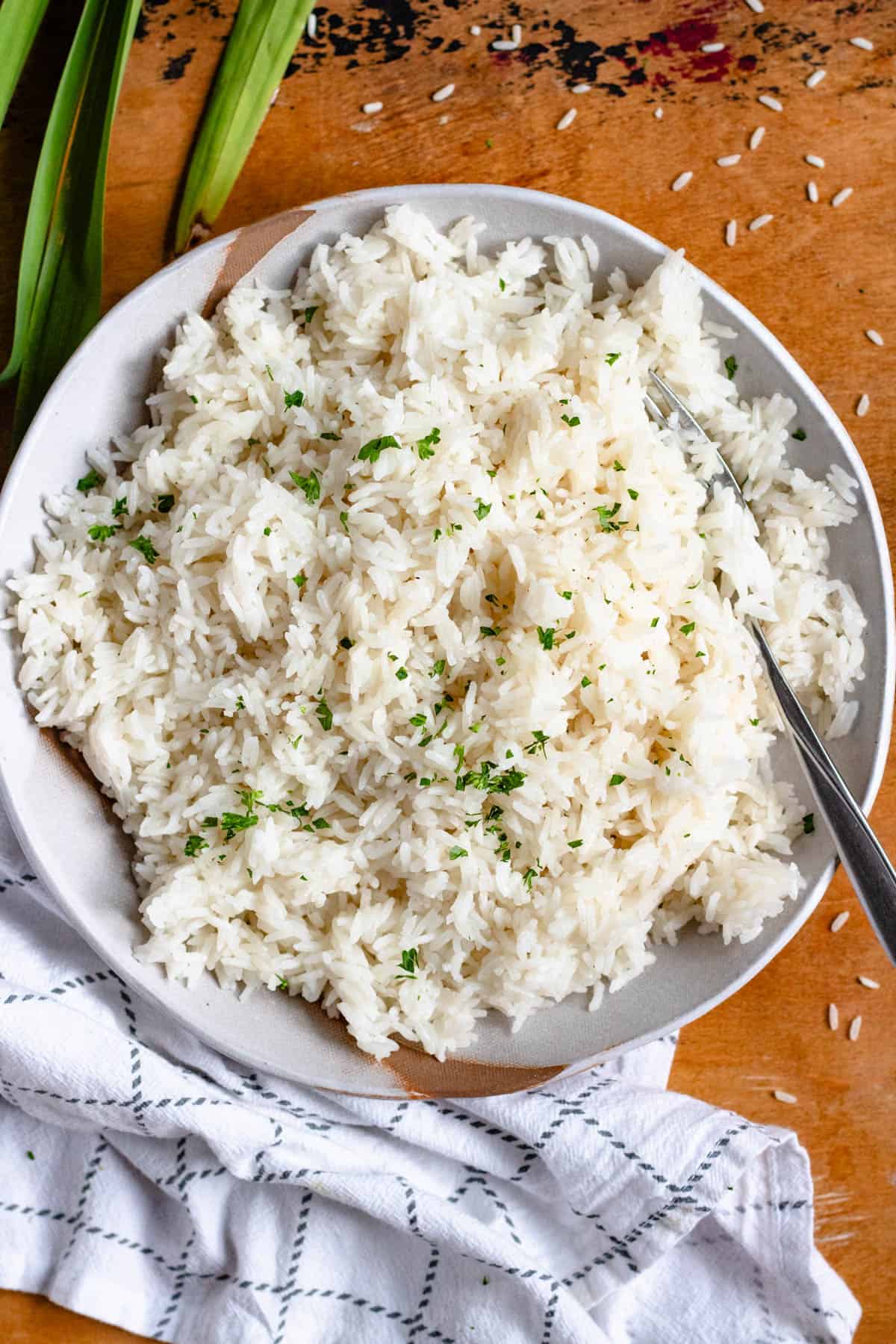 Top image of a bowl of coconut rice garnished with chopped parsley, with pandan leaves in the background.