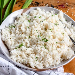 A bowl of coconut rice garnished with chopped parsley, with pandan leaves in the background.