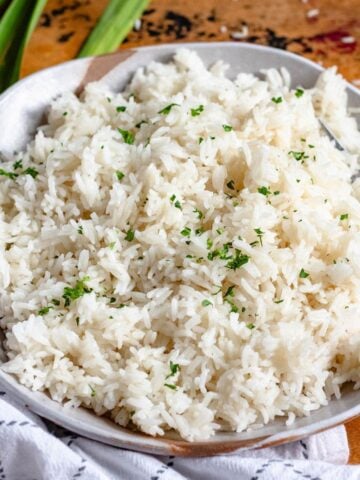A bowl of coconut rice garnished with chopped parsley, with pandan leaves in the background.