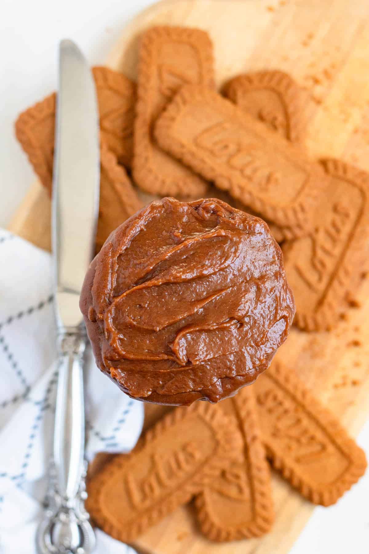 A jar of rich, creamy cookie butter with a pile of Lotus Biscoff cookies on a wooden board.
