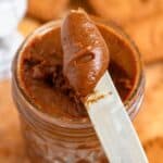 A close-up of creamy cookie butter being scooped from a jar with a butter knife.
