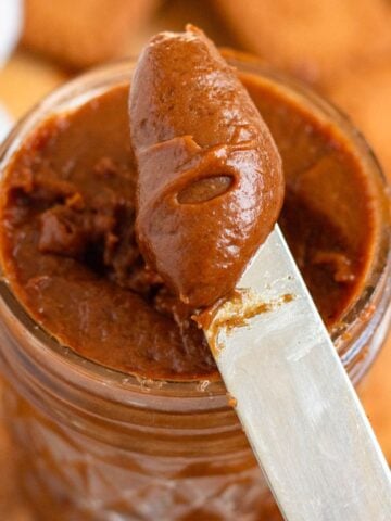 A close-up of creamy cookie butter being scooped from a jar with a butter knife.