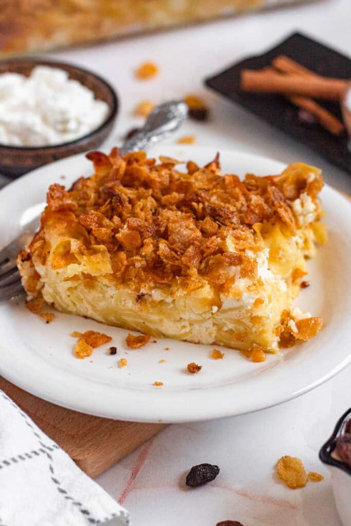 A close-up of a baked Noodle Kugel slice topped with a crunchy golden cornflake crust on a white plate.
