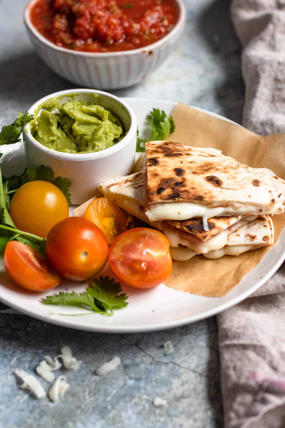 Sincronizadas cut into fours and served on a plate along with cherry tomatoes and a small bowl with guacamole.