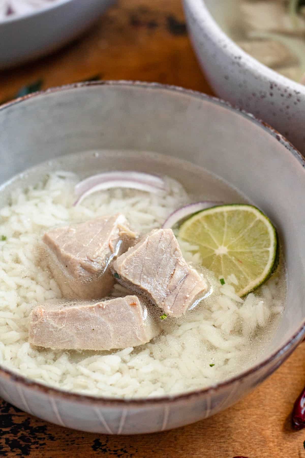 Close-up image of a bowl of Garudhiya, a Maldivian fish soup served with rice, red onions, and lime.