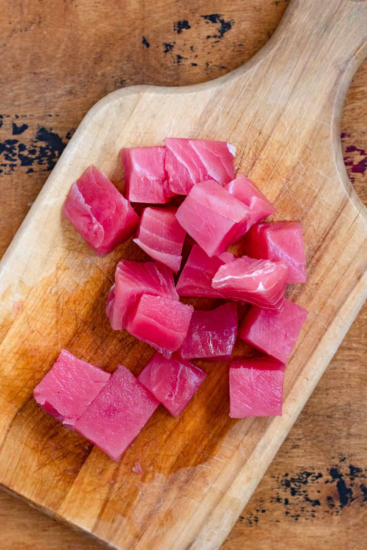 Cubed pieces of fresh tuna on a wooden chopping board.