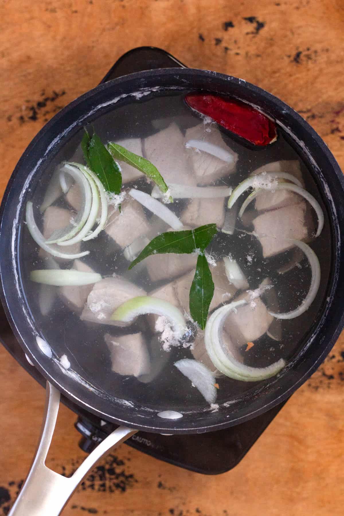 Tuna, onion, curry leaves, and chili pepper simmering in a pot of boiling broth.