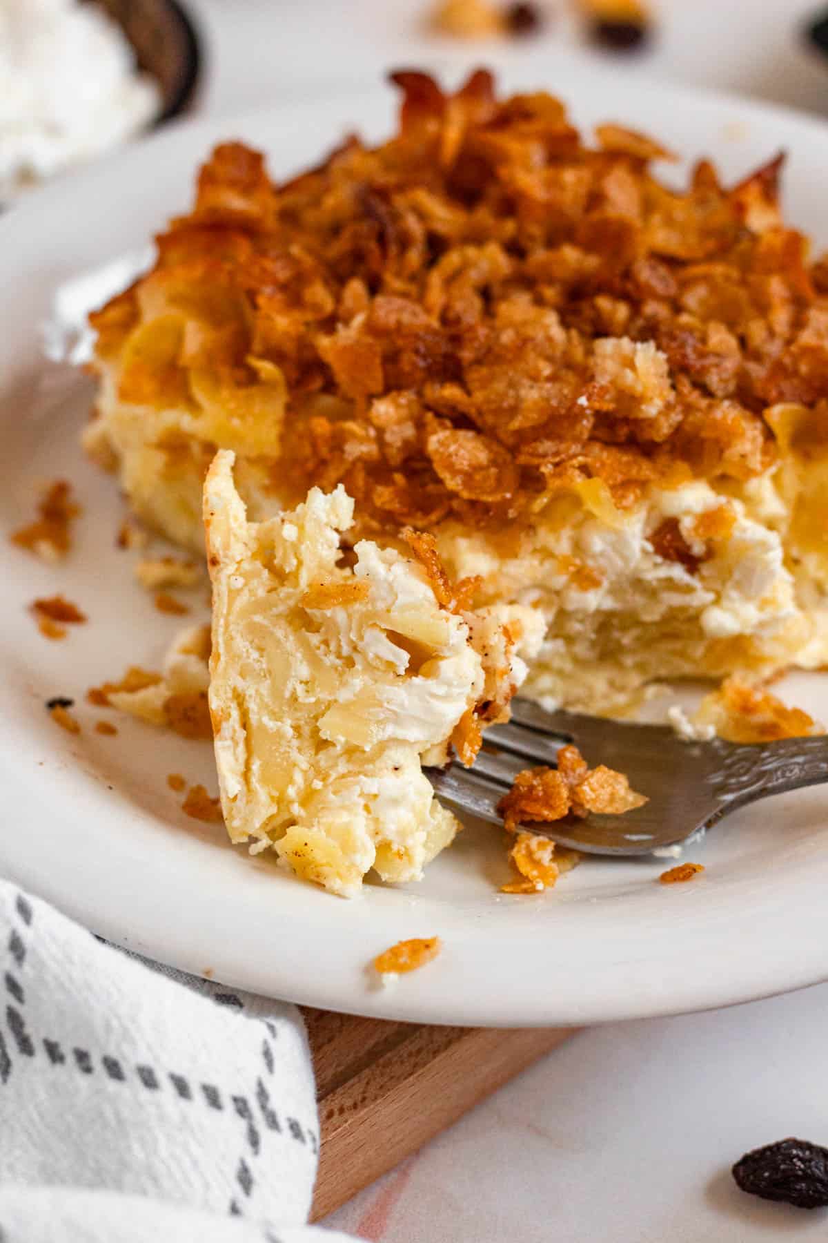 A close-up of a forkful of creamy noodle kugel with a crispy cornflake topping on a plate.