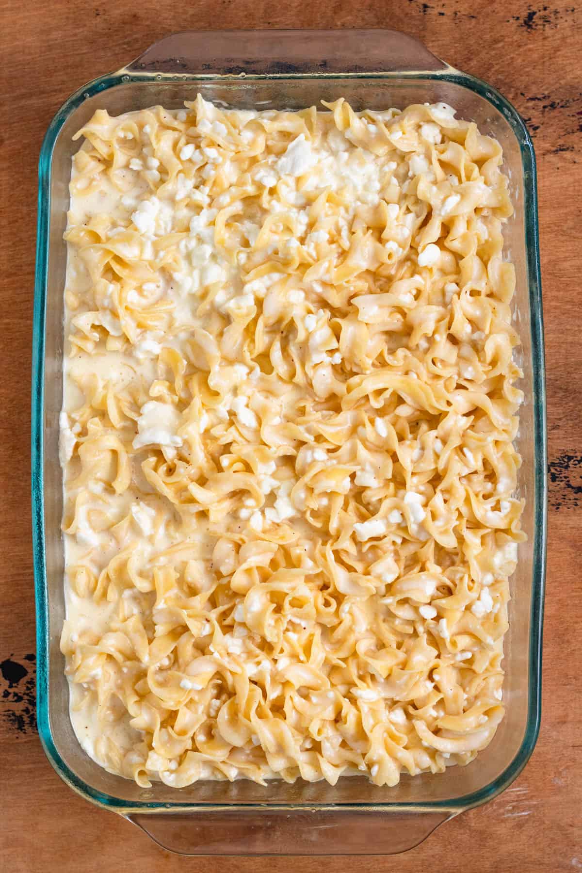 Noodles coated in custard being transferred into a baking dish.