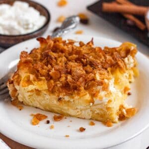 A close-up of a baked noodle kugel slice topped with a crunchy golden cornflake crust on a white plate.