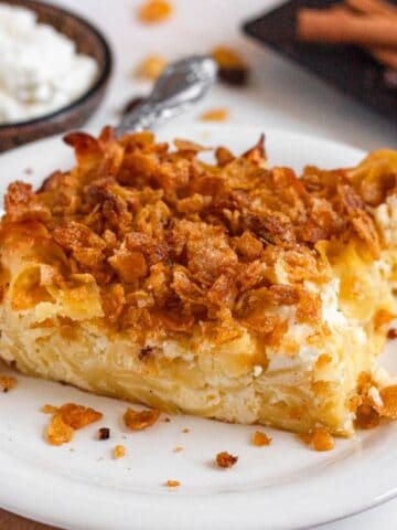 A close-up of a baked noodle kugel slice topped with a crunchy golden cornflake crust on a white plate.