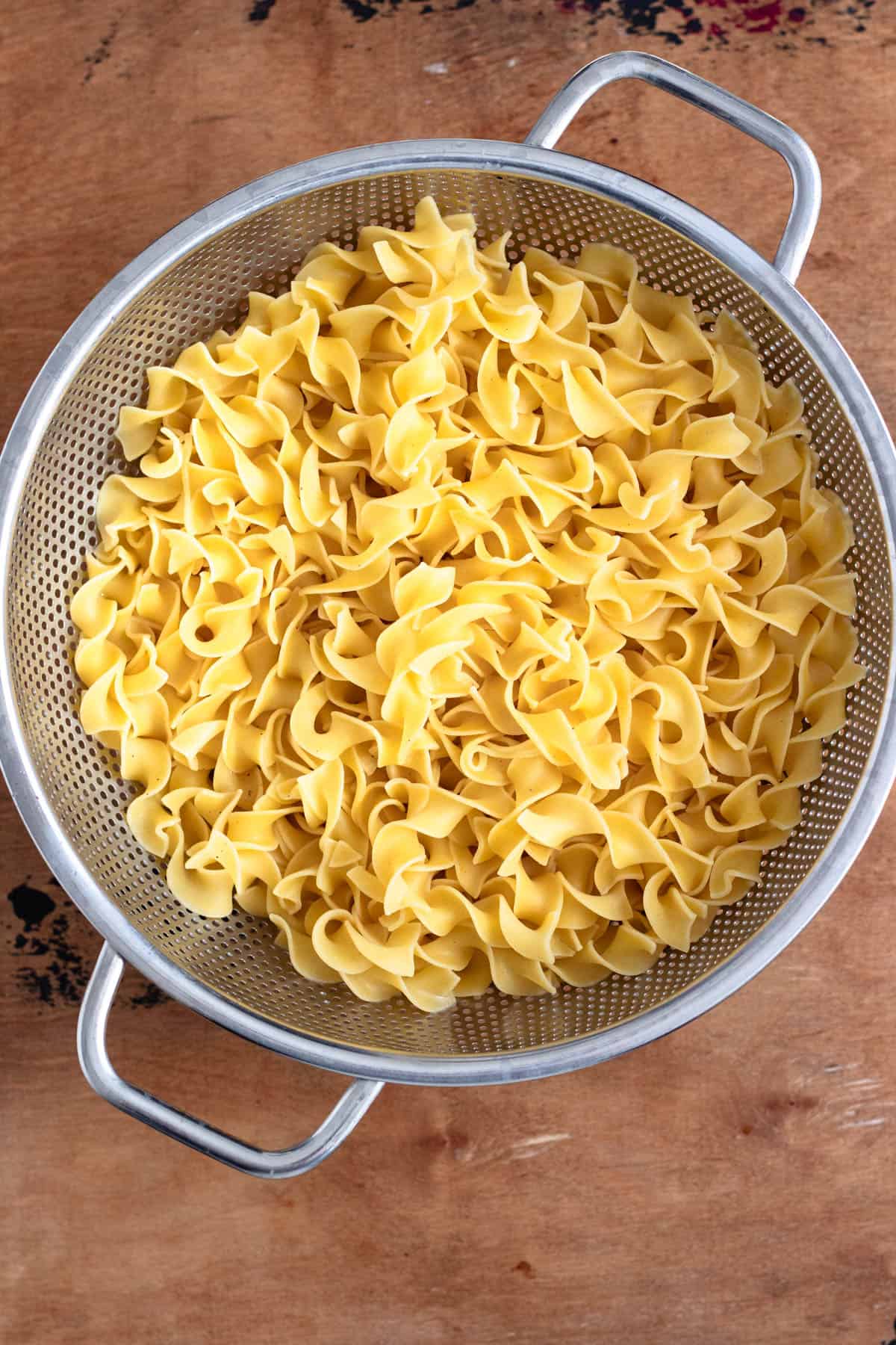 Cooked egg noodles draining in a mesh strainer.