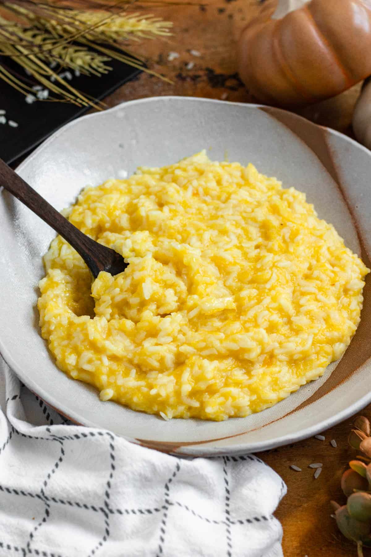 A bowl of creamy pumpkin rice with a wooden spoon.